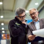 Ein Manager und ein Mitarbeiter besprechen Dokumente in einer Industriehalle