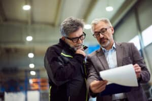Ein Manager und ein Mitarbeiter besprechen Dokumente in einer Industriehalle