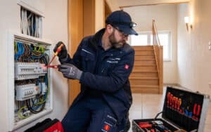 Ein Elektriker prüft mit einem Spannungsprüfer die Leitungen in einem offenen Sicherungskasten